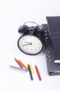 Stack of book with ticking vintage clock and colorful crayon on white table.