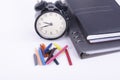 Stack of book with ticking vintage clock and colorful crayon on white table.