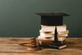Stack of books, academic cap and gavel on wooden surface