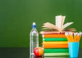 Stack of books with apple, bottle of water and pencils near empty green chalkboard. Sample for text Royalty Free Stock Photo