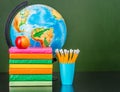 Stack of books with apple, pencils and globe near empty green chalkboard. Space for text Royalty Free Stock Photo