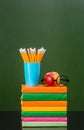 Stack of books with apple and pencils near empty green chalkboard Royalty Free Stock Photo