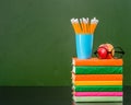 Stack of books with apple and pencils near empty green chalkboard Royalty Free Stock Photo