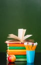 Stack of books with apple and pencils near empty green chalkboard Royalty Free Stock Photo