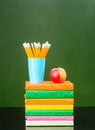 Stack of books with apple and pencils near empty green chalkboard Royalty Free Stock Photo