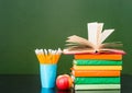 Stack of books with apple and pencils near empty green chalkboard. Sample for text Royalty Free Stock Photo