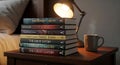 Stack of books on a bedside table next to a steaming mug and lamp providing cozy reading atmosphere for relaxation and study Royalty Free Stock Photo