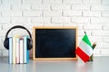 Stack of books, blackboard and flag of Italy on desk. Italian language learning concept