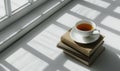 Stack of books with a cup of tea on a light gray table, soft shadows from window Royalty Free Stock Photo
