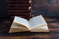 A stack of books with a dark red hard cover one another and open book on a wooden table against the background of brown brick wall Royalty Free Stock Photo