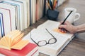 Stack of books education background, female hand makes notes near open textbook. Glasses, pens and pencils in holder, cup of tea Royalty Free Stock Photo