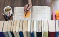 Stack of books education background, female hand makes notes near open textbook. Glasses, pens and pencils in holder, cup of tea