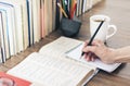 Stack of books education background, female hand makes notes in open notebook. Glasses, pens and pencils in holder, cup of tea Royalty Free Stock Photo