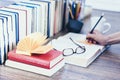 Stack of books education background, open book, female hand with pencil, glasses, and cup of tea with lemon Royalty Free Stock Photo