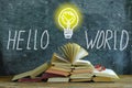 Stack of books in front of a blackboard, drawing of a lightbulb and slogan hello world,knowledge, education and social integration