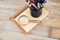 On a stack of books in front of a blackboard full of mathematical formulas, a pen holder full of colored pencils and a magnifying