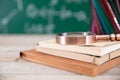 On a stack of books in front of a blackboard full of mathematical formulas, a pen holder full of colored pencils and a magnifying