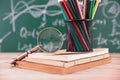 A stack of books in front of a blackboard full of mathematical formulas and a red apple on the books and a pen holder full of colo