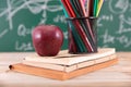 A stack of books in front of a blackboard full of mathematical formulas and a red apple on the books and a pen holder full of colo Royalty Free Stock Photo
