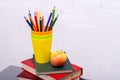 A stack of books and a glass with pencils on the table close-up