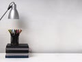 Stack of books,lamp and pencil holder full of pencils on the white table against bright wall.Empty space Royalty Free Stock Photo