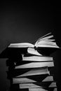 A stack of books with one open book on top, pages slightly fanned out, in a black and white setting with dramatic lighting and Royalty Free Stock Photo