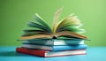 Stack of books with open book on top showing pages. Colorful books rest on blue surface against green background. Education and Royalty Free Stock Photo