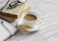 A stack of books, open clean notepad, glasses and a cup of cocoa on a white wooden table.