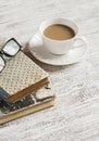 A stack of books, open clean notepad, glasses and a cup of cocoa on a white wooden table.