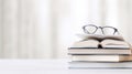 A stack of books with a pair of glasses on a white background. The books are colorful and of different sizes. The