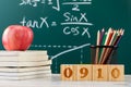 Stack of books with pencil holder, apple, and 0910 wooden numbers against a chalkboard Royalty Free Stock Photo