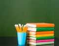 Stack of books with pencils near empty green chalkboard. Sample for text Royalty Free Stock Photo