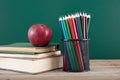 A stack of books with a red apple and a pen holder full of colored pencils in front of the blackboard Royalty Free Stock Photo