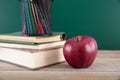 A stack of books with a red apple and a pen holder full of colored pencils in front of the blackboard Royalty Free Stock Photo