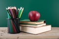 A stack of books with a red apple and a pen holder full of colored pencils in front of the blackboard Royalty Free Stock Photo