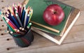 A stack of books with a red apple and a pen holder full of colored pencils in front of the blackboard Royalty Free Stock Photo