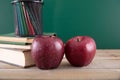 A stack of books and two red apples in front of the blackboard and a pen holder filled with colored pencils Royalty Free Stock Photo