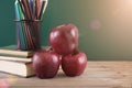 A stack of books and two red apples in front of the blackboard and a pen holder filled with colored pencils Royalty Free Stock Photo