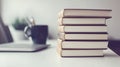 A Stack of Books on a White Table with a Laptop and Cup in the Background Royalty Free Stock Photo
