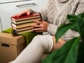 A stack of books in women`s hands. A girl in a knitted sweater is surrounded by many books
