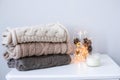 A stack of brown and beige sweaters and scarf with garland lights, candle. Cozy interior details Royalty Free Stock Photo
