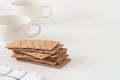 Stack of brown rye crispy bread Swedish crackers with two cups and piece of cloth on white background with space for text Royalty Free Stock Photo