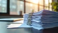 Stack of business documents on office desk. Papers in metal binder. Office workspace with laptop and window in background. Royalty Free Stock Photo