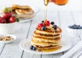 A stack of buttermilk pancakes served with berries and bananas with syrup being poured on top. Royalty Free Stock Photo