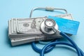 Stack of cash dollars and credit card with stethoscope on blue background. The concept of medical strechevka or expensive medicine Royalty Free Stock Photo