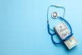 Stack of cash dollars and stethoscope on blue background. The concept of medical strechevka or expensive medicine, doctors salary.