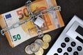 A stack of cash with 50 euro banknotes is locked with a chain and padlock next to a calculator and coins Royalty Free Stock Photo
