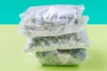 A stack of cellophane bags with frozen vegetables on green background close-up.