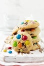 Stack of children cookies with colorful chocolate candies in a sugar glaze on a white light wooden background. Selective focus