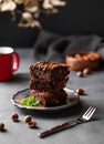 A stack of chocolate brownies with mint and hazelnuts on a dark background with cup of coffee and nuts